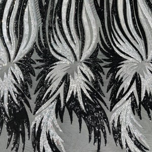 May include: Black and silver sequined fabric with a wavy, feather-like pattern. The fabric is made of a mesh material and is perfect for adding a touch of sparkle to any project.