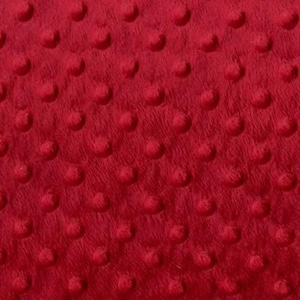 May include: Close-up of a red, textured fabric with a raised dot pattern. The fabric has a soft, plush appearance, with the dots evenly spaced across the surface. The color is a deep, vibrant red.