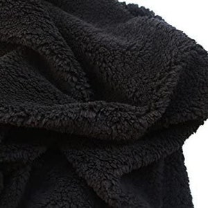 Pode incluir: Uma manta preta e fofa feita de tecido macio e felpudo. A manta está dobrada e drapeada sobre si mesma, mostrando a textura do material.