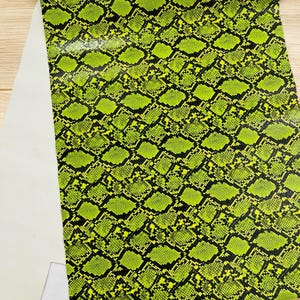 Op de afbeelding: Een close-up van een groene en zwarte stof met een slangenhuidpatroon. De stof heeft een glanzende, bijna natte uitstraling.
