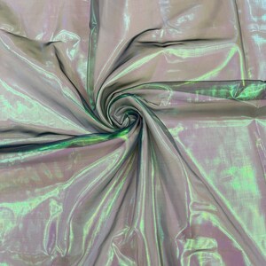 May include: A sheer iridescent fabric with a green and purple sheen. The fabric is draped and folded, creating a swirling pattern.