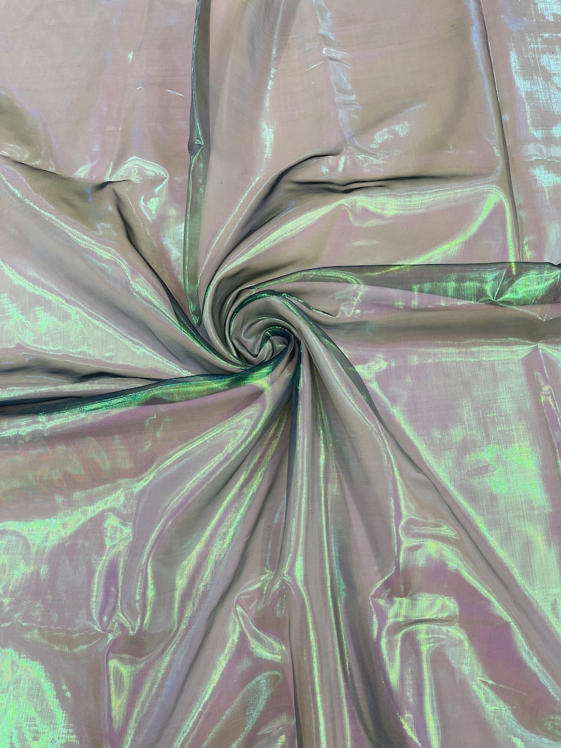 May include: A sheer iridescent fabric with a green and purple sheen. The fabric is draped and folded, creating a swirling pattern.
