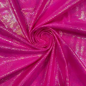 Puede incluir: Una tela de color rosa intenso vibrante con una textura reflectante e iridiscente similar a la piel de serpiente. El material está recogido en una espiral central, creando pliegues profundos y reflejos que resaltan el acabado metálico.