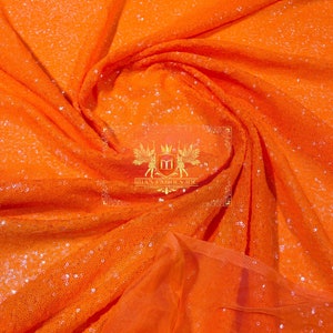 May include: Orange sequin fabric with a sheer mesh backing. The fabric is draped and folded to show the texture of the sequins.