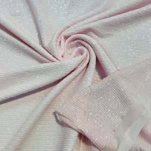 May include: Pale pink sequin fabric with a soft, flowing drape. The fabric is covered in small, reflective sequins that catch the light. The texture is smooth and the fabric appears to be lightweight, suitable for apparel or decorative projects.