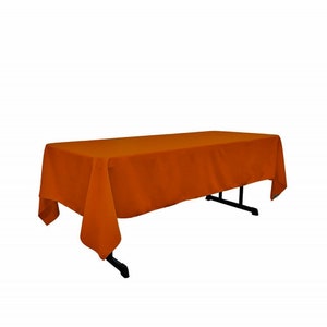 May include: A burnt orange rectangular tablecloth draped over a table. The tablecloth has a smooth, even texture.