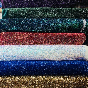 May include: A stack of eight rolls of sparkly fabric in various colors, including red, purple, green, blue, white, gold, and silver.