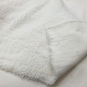 May include: A white faux fur fabric with a smooth, woven backing. The fabric is soft and fluffy, with a luxurious feel.