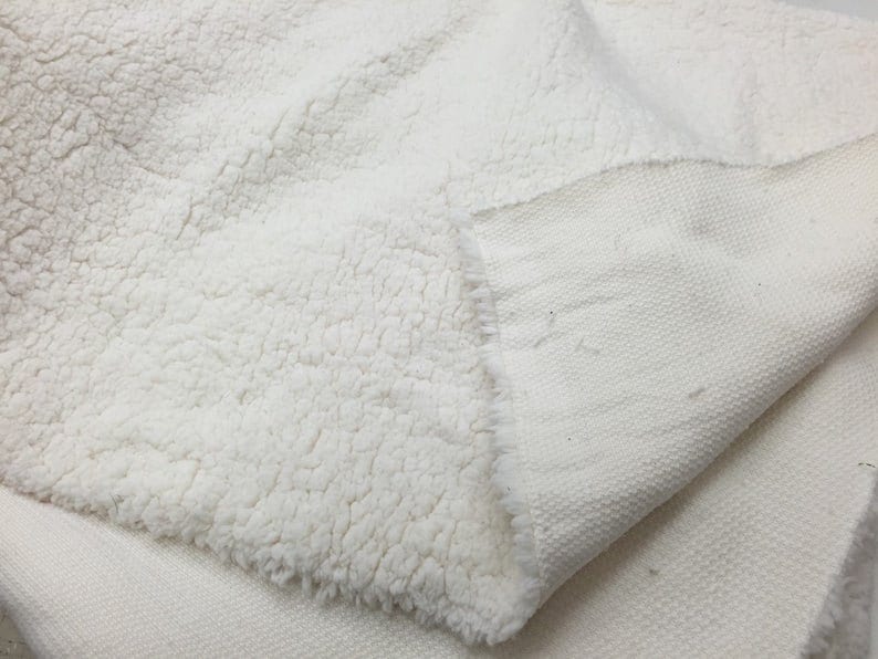 May include: A white faux fur fabric with a smooth, woven backing. The fabric is soft and fluffy, with a luxurious feel.