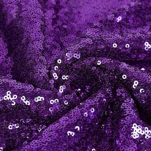 Pode incluir: Tecido de lantejoulas roxo com uma visão de perto das lantejoulas. O tecido é texturizado e brilhante.