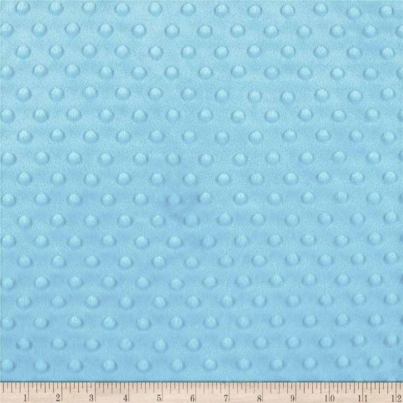 May include: A close-up of a light blue fabric with a textured pattern of small, raised circles. The fabric is soft and plush, perfect for baby blankets or other soft goods.