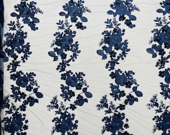 May include: Navy blue floral embroidered lace fabric with a delicate mesh background. The fabric features a repeating pattern of 3D floral motifs with small pearl-like embellishments.
