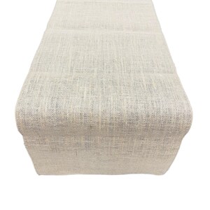 Könnte beinhalten: Ein natürlicher beigefarbener Tischläufer aus Jute. Der Läufer besteht aus einem gewebten Stoff mit leicht rauer Textur.