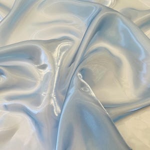 Peut inclure: Gros plan sur un tissu bleu clair et blanc à la texture soyeuse et chatoyante. Le tissu est drapé en plis souples, créant une apparence fluide et élégante. Le dégradé de couleurs passe d'un blanc pâle à un bleu doux.