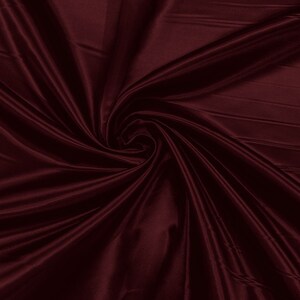 May include: A close-up of a deep burgundy satin fabric with soft, flowing folds.