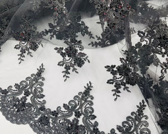 May include: Black beaded lace fabric with a floral design. The lace has a scalloped edge and is made of a sheer mesh material.