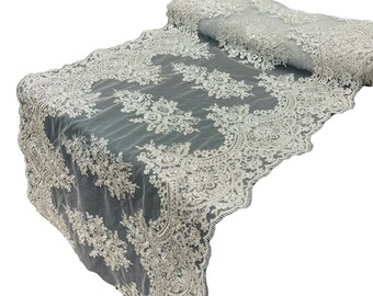 May include: A white lace table runner with a beaded design. The runner is rolled up and has a scalloped edge.