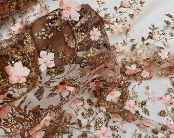 Puede incluir: Delicada tela de encaje floral rosa rubor con purpurina dorada y lentejuelas. La tela presenta flores 3D con centros de perlas y bordados dorados intrincados, ideal para novias u ocasiones especiales.