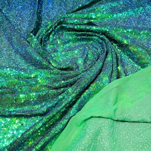 Puede incluir: Paillettes iridiscentes verdes y azules sobre una tela de malla. La tela está doblada y drapeada para mostrar las lentejuelas y el respaldo de malla.