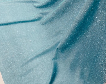 May include: A light blue fabric with a sparkly, glittery texture. The fabric is folded and draped on a white surface.
