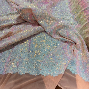 May include: A close-up of iridescent blue and pink sequins on a sheer pink mesh fabric. The sequins are small and densely packed, creating a shimmering effect.