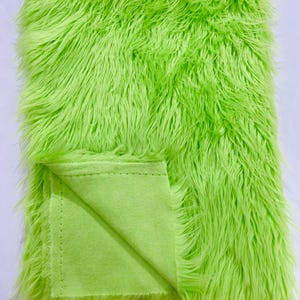May include: A bright green faux fur fabric with a soft, plush texture. The fabric is folded in half, revealing a green cotton backing.