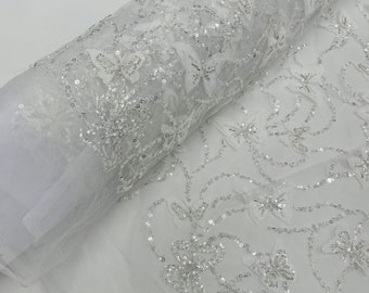 May include: White tulle fabric with silver sequins and butterfly embellishments. The fabric is rolled up and the sequins and butterflies are visible on the surface.