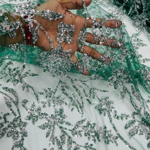 May include: Green mesh fabric with silver glitter floral embroidery. The fabric is sheer and has a delicate, feminine look.