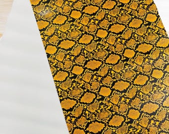 Puede incluir: Tela con estampado de piel de serpiente amarilla y negra. La tela tiene un aspecto brillante, casi mojado.