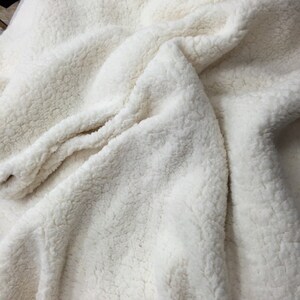 May include: A close-up of a white faux fur fabric. The fabric has a soft, fluffy texture and is perfect for making blankets, throws, or other cozy items.