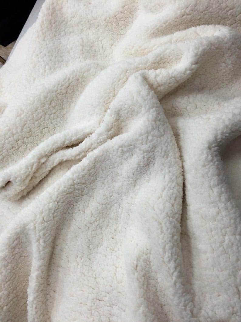 May include: A close-up of a white faux fur fabric. The fabric has a soft, fluffy texture and is perfect for making blankets, throws, or other cozy items.