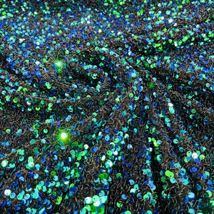 May include: Close-up of a fabric with blue and green sequins on a black background.
