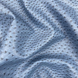 Puede incluir: Primer plano de una tela azul claro con superficie texturizada. La tela presenta un patr&oacute;n de peque&ntilde;as protuberancias oscuras, espaciadas uniformemente. El material parece suave y flexible, con pliegues y sombras suaves.