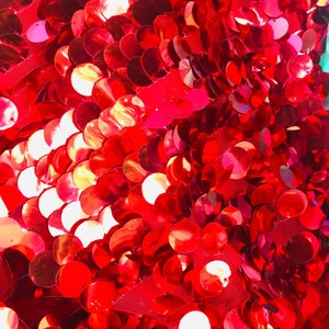 May include: Red sequin fabric with a close-up view of the sequins. The sequins are round and have a shiny finish.