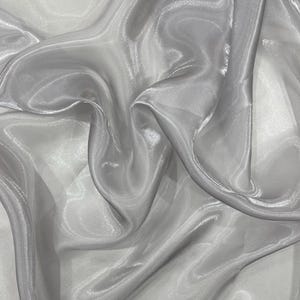 Peut inclure: Gros plan sur un tissu fluide et transparent dans des tons de gris et de blanc. Le tissu a un éclat subtil, la lumière se reflétant sur les plis, créant des reflets et des ombres. Le matériau semble doux et délicat.