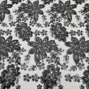May include: Black floral lace fabric with sequins. The lace features a repeating pattern of large and small flowers.