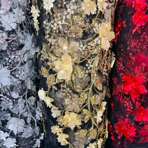 May include: Three rolls of black mesh fabric with different colored 3D floral embellishments. The fabric on the left has silver sequins and white flowers. The middle fabric has gold sequins and cream flowers. The fabric on the right has red flowers.