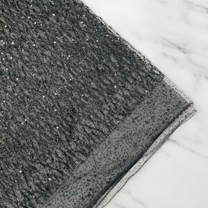 May include: Black sequined fabric with a subtle shimmer. The fabric has a fine mesh texture and is perfect for crafting or sewing projects.