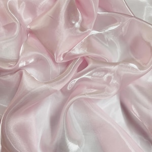 Peut inclure: Gros plan sur un tissu fluide et translucide rose clair. Le tissu présente des reflets et des ombres, créant de la profondeur et du mouvement. Le matériau semble léger et soyeux, avec un éclat subtil. Idéal pour la couture ou la décoration.