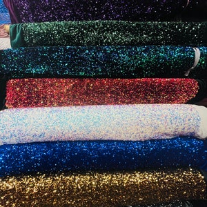 May include: A stack of different colored sequined fabrics. The fabrics are arranged in a rainbow pattern, starting with red and ending with green. The sequins are small and sparkly, and they create a shimmering effect.