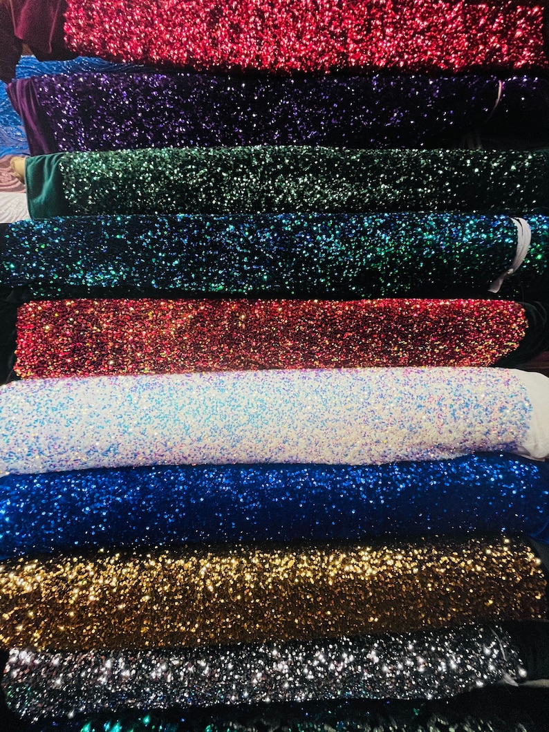 May include: A stack of different colored sequined fabrics. The fabrics are arranged in a rainbow pattern, starting with red and ending with green. The sequins are small and sparkly, and they create a shimmering effect.