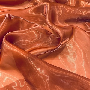 May include: Close-up of flowing, translucent fabric in shades of orange and peach. The fabric has a subtle sheen and a rippled texture, with light reflecting off the folds and creating highlights. The overall effect is soft and ethereal.