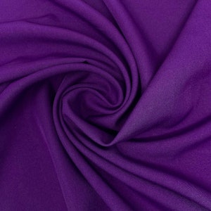 Può includere: Un primo piano di un tessuto viola scuro con una texture morbida e liscia. Il tessuto è piegato e drappeggiato, creando un aspetto lussuoso ed elegante.