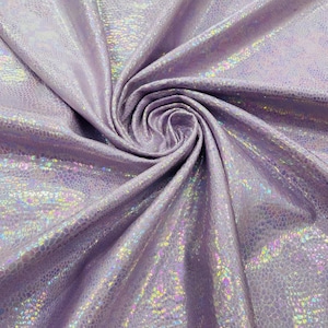 Puede incluir: Una tela de color lavanda con un patrón holográfico de piel de serpiente que refleja la luz con colores iridiscentes de arcoíris. El material está recogido en un remolino central, mostrando la superficie texturizada y el acabado metálico brillante.