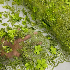 May include: Green floral lace fabric with sequins and 3D flowers. The fabric has a mesh base and is embellished with green sequins and 3D flowers.