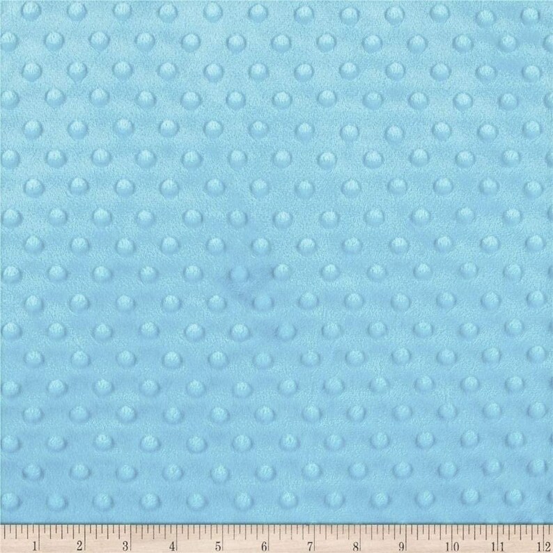 May include: A close-up of a light blue fabric with a textured pattern of small, raised circles. The fabric is soft and plush, perfect for baby blankets or other soft goods.