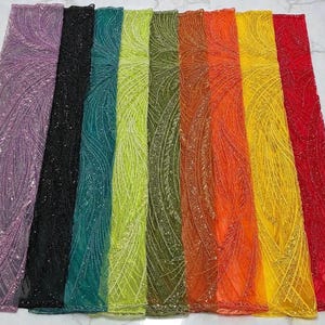 May include: A collection of colorful, shimmering fabrics. The fabrics are arranged side-by-side, showcasing a spectrum of colors including purple, black, teal, green, orange, yellow, and red. Each fabric has a detailed, textured pattern with sparkling embellishments.