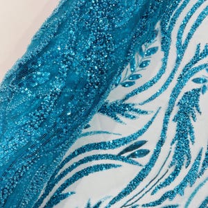 May include: A sheer white fabric featuring an intricate, swirling pattern of teal sequins and beads. The design consists of elongated, leaf-like shapes and flowing lines that create a dense, textured surface across the semi-transparent material.