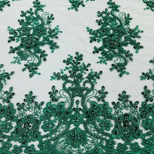 May include: Emerald green beaded lace fabric with a floral pattern. The lace is delicate and intricate, with small beads scattered throughout. The fabric is perfect for adding a touch of elegance to any project.