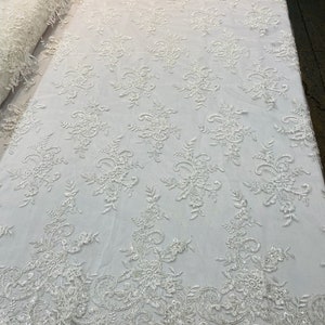 May include: White beaded lace fabric with a floral pattern. The lace has a delicate, intricate design with small, white beads.